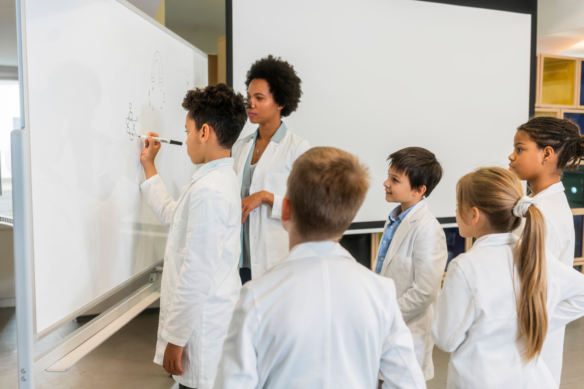 Diverse schoolchildren with teacher work together on science project, using microscope