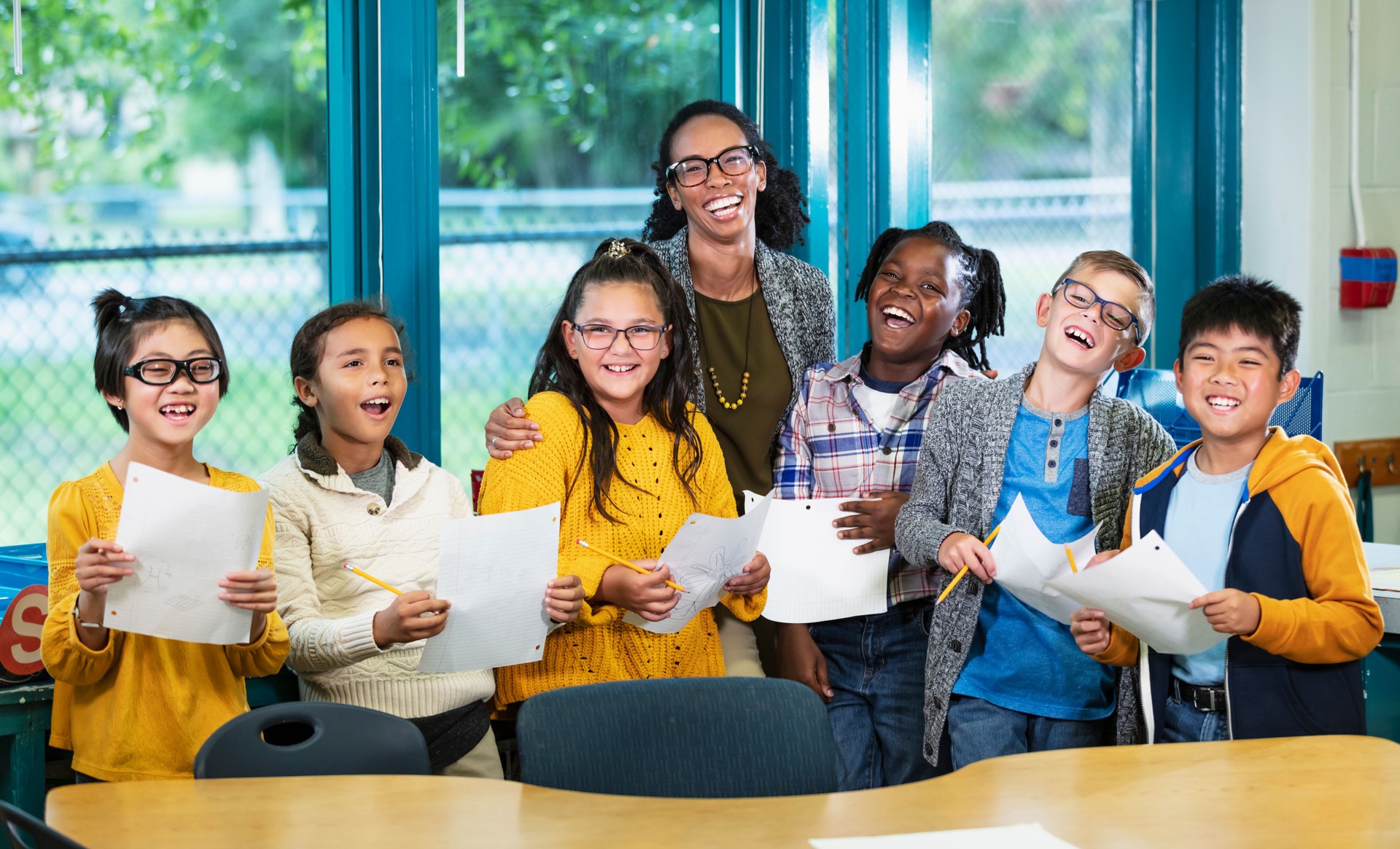 Multiracial teacher, elementary students smile at camera